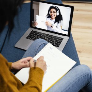 Une femme souriante et engagée, assise devant son ordinateur portable, participe activement à un cours de langue en ligne. Elle interagit avec passion avec son enseignante virtuelle, symbolisant l'engagement et la connexion dans l'apprentissage linguistique en ligne.