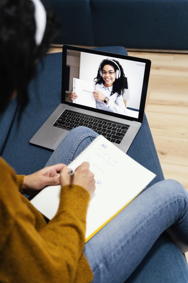Une femme souriante et engagée, assise devant son ordinateur portable, participe activement à un cours de langue en ligne. Elle interagit avec passion avec son enseignante virtuelle, symbolisant l'engagement et la connexion dans l'apprentissage linguistique en ligne.